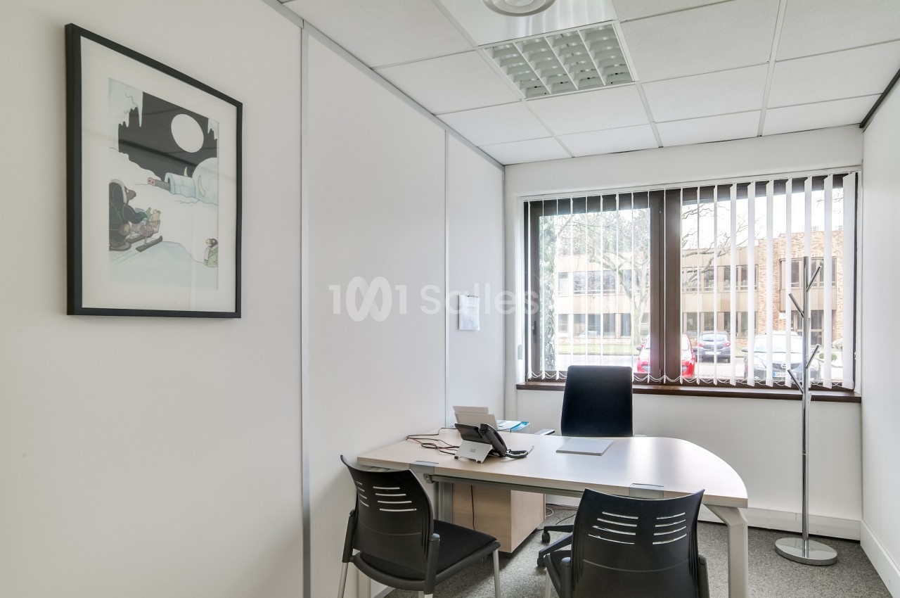 Bureau lumineux avec un bureau blanc, trois chaises, un téléphone, une fenêtre avec stores et un tableau au mur.