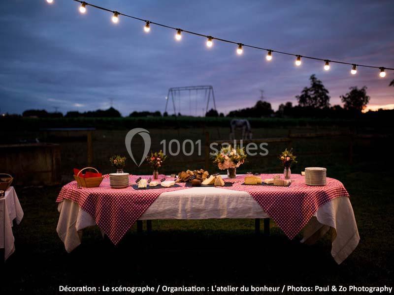 Table dressée en extérieur avec nappes à carreaux rouges, plats variés et guirlande lumineuse au crépuscule.