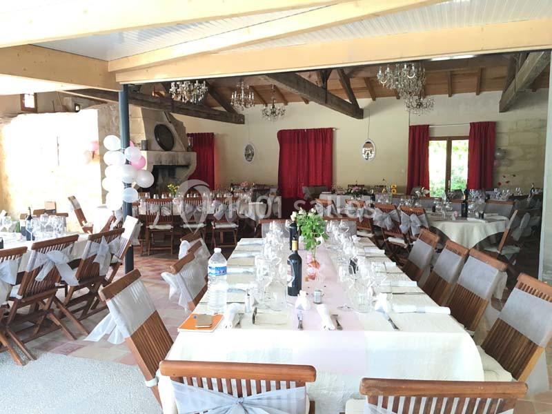 Salle de réception décorée avec des tables dressées, chaises ornées de nœuds et ballons roses près d'une cheminée.