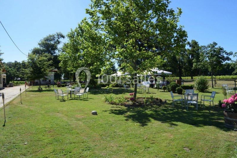 Jardin verdoyant avec tables et chaises disposées sous des arbres, entouré de vignes et de fleurs.