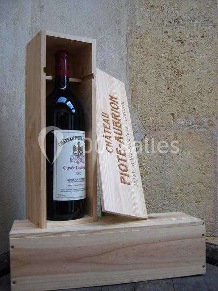 Bouteille de vin rouge dans une caisse en bois ouverte, posée contre un mur en pierre.