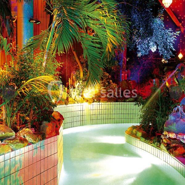Piscine intérieure entourée de plantes tropicales et éclairée par des lumières colorées.