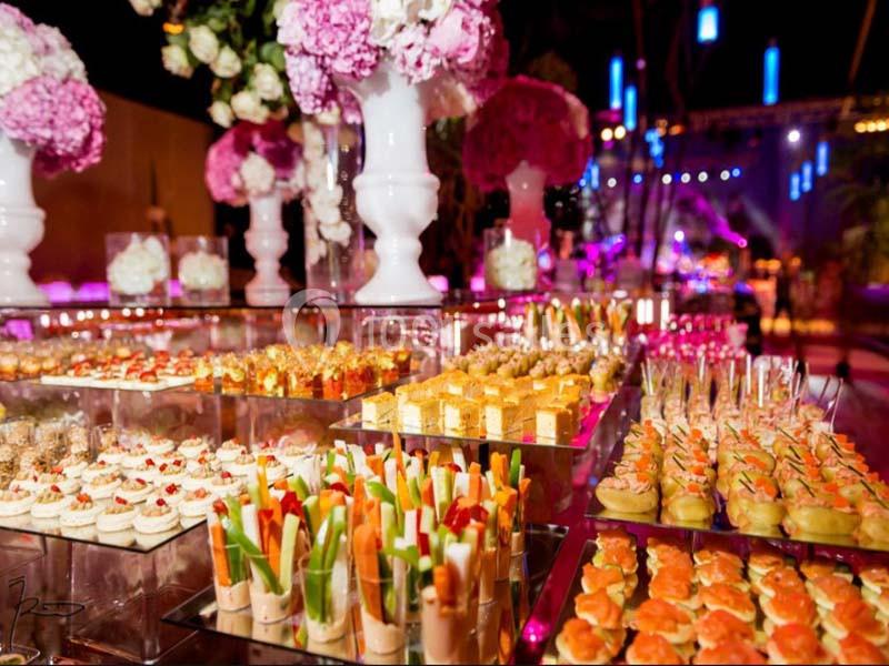 Buffet élégant avec verrines, desserts et fleurs roses en arrière-plan dans une ambiance festive et lumineuse.