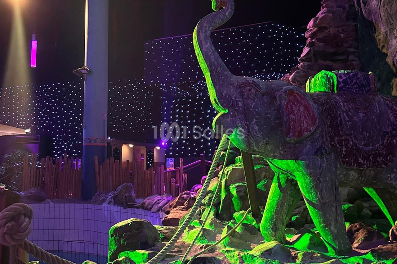 Statue d'éléphant en pierre éclairée par des lumières vertes, entourée de cordes et de décorations dans un espace intérieur…