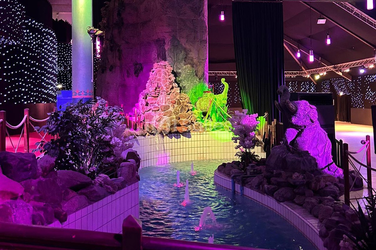 Décor intérieur avec un ruisseau artificiel, des rochers, des plantes et un éclairage coloré violet et vert.