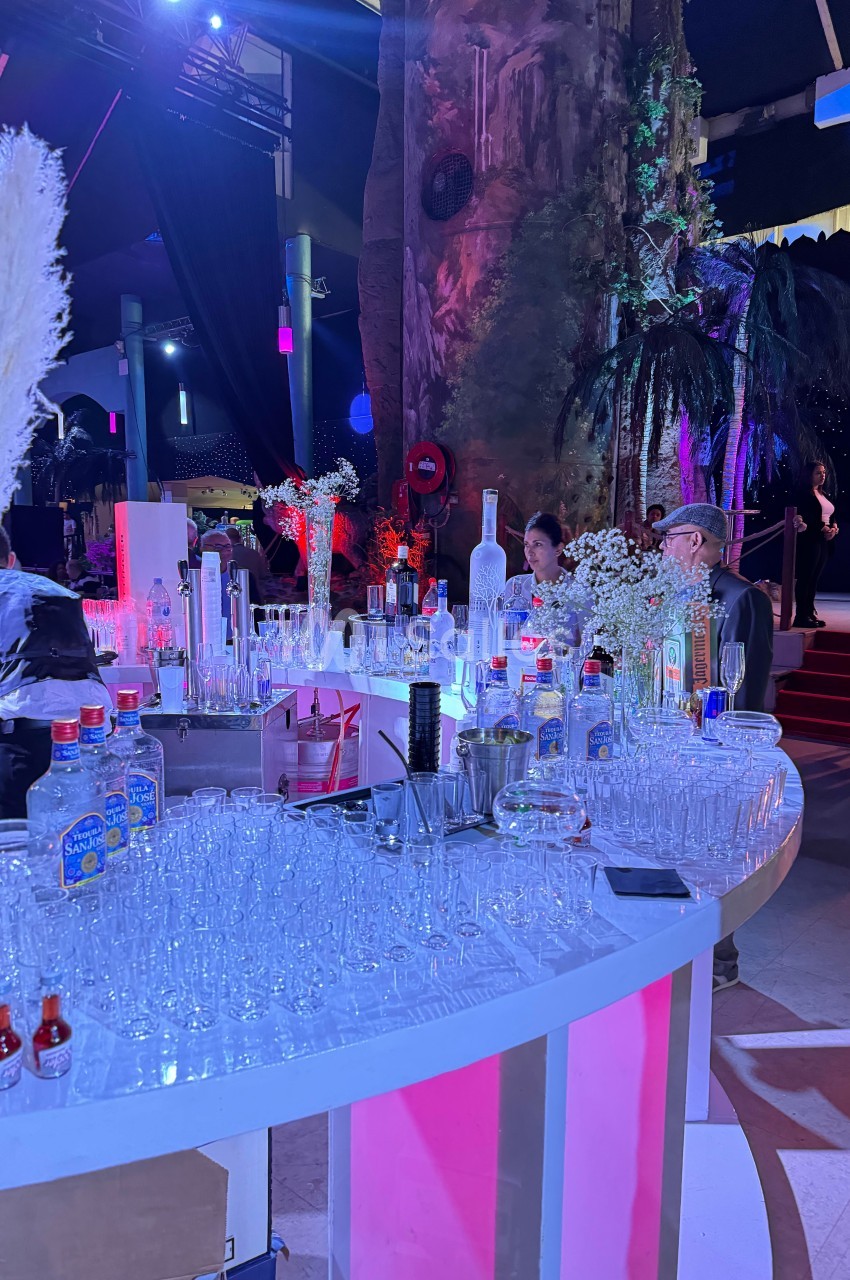 Bar circulaire éclairé avec des verres, bouteilles et décorations, dans un espace événementiel à l'ambiance lumineuse.