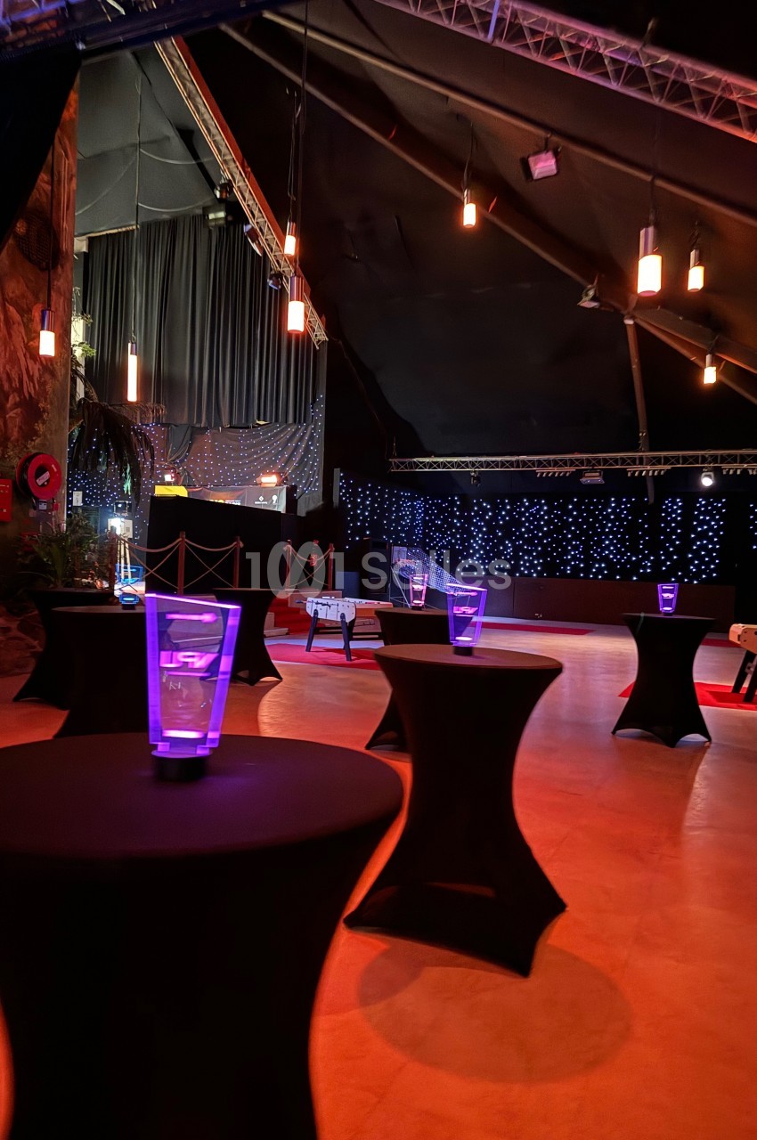 Salle de réception avec tables hautes noires, verres lumineux et éclairage tamisé dans une ambiance festive.
