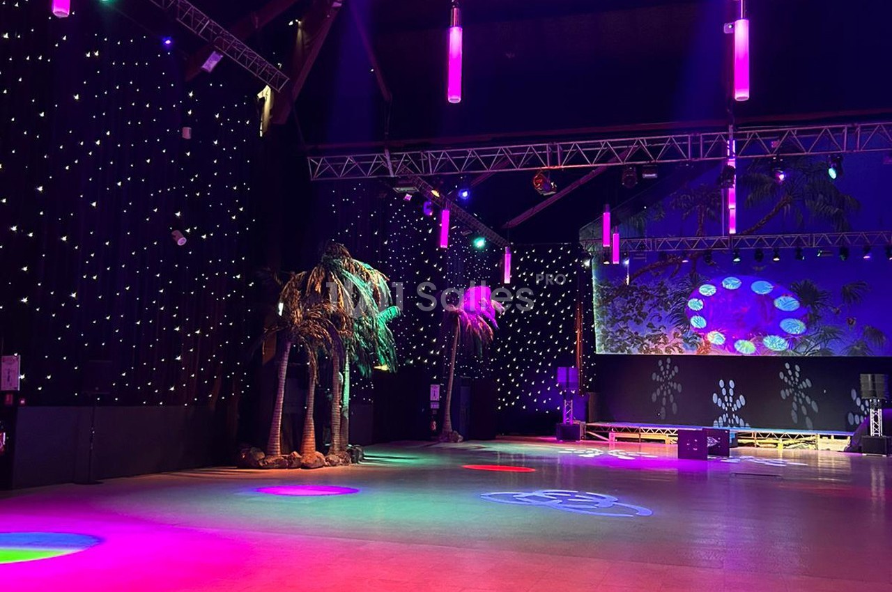 Salle de spectacle avec éclairage coloré, palmiers décoratifs et murs ornés de lumières étoilées.