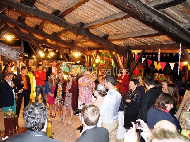 Groupe de personnes réunies dans un espace couvert décoré, observant un couple au centre lors d'un événement festif.