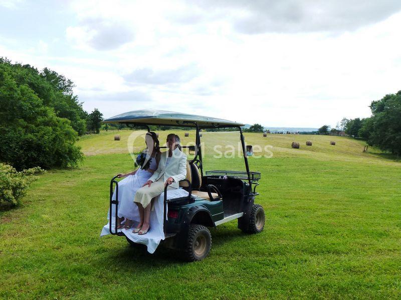 Un couple en tenue de mariage assis à l'arrière d'une voiturette de golf dans un champ verdoyant.