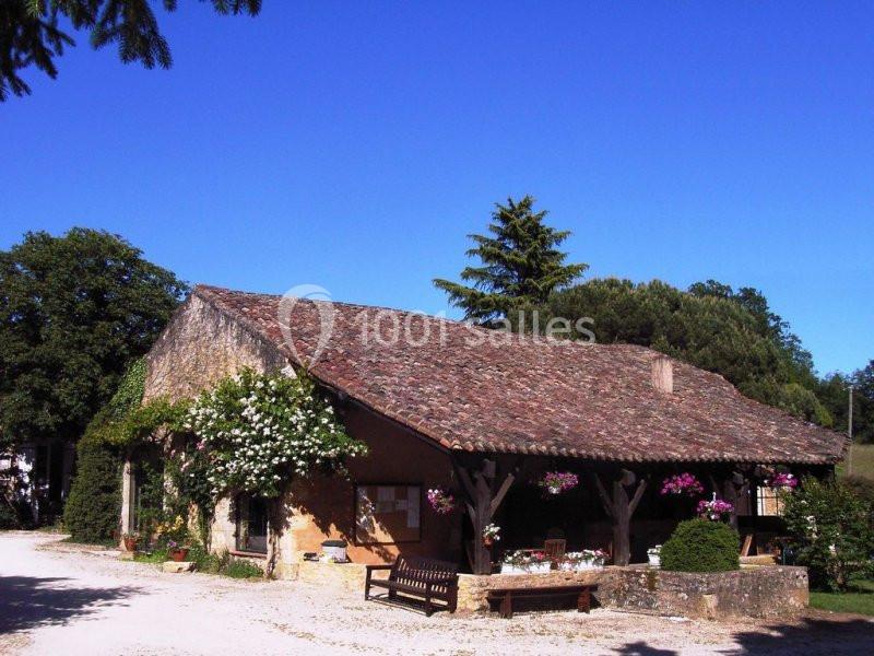 Maison en pierre avec toit en tuiles, entourée de fleurs et de végétation, sous un ciel bleu dégagé.