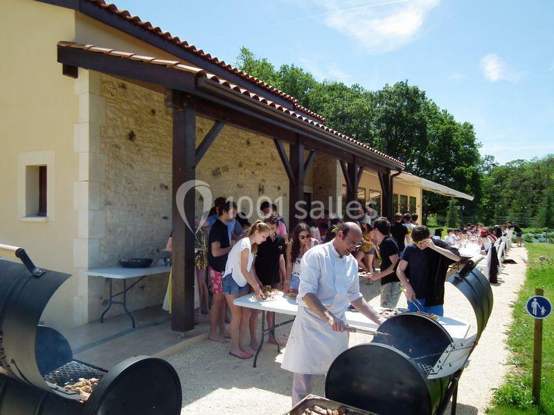 Des personnes font la queue pour un barbecue en plein air sous un auvent près d'un bâtiment en pierre.