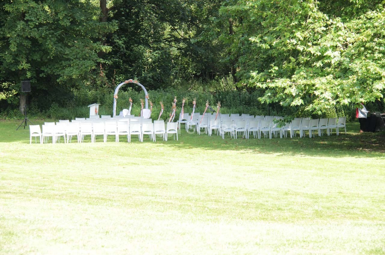 Chaises blanches disposées en extérieur devant une arche décorée, entourées de verdure dans un cadre naturel.