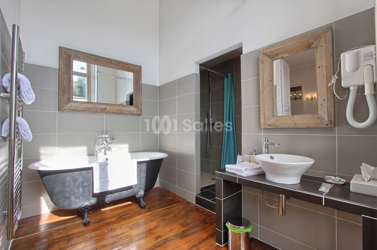 Salle de bain lumineuse avec baignoire sur pieds, lavabo moderne, miroir encadré en bois et douche ouverte.