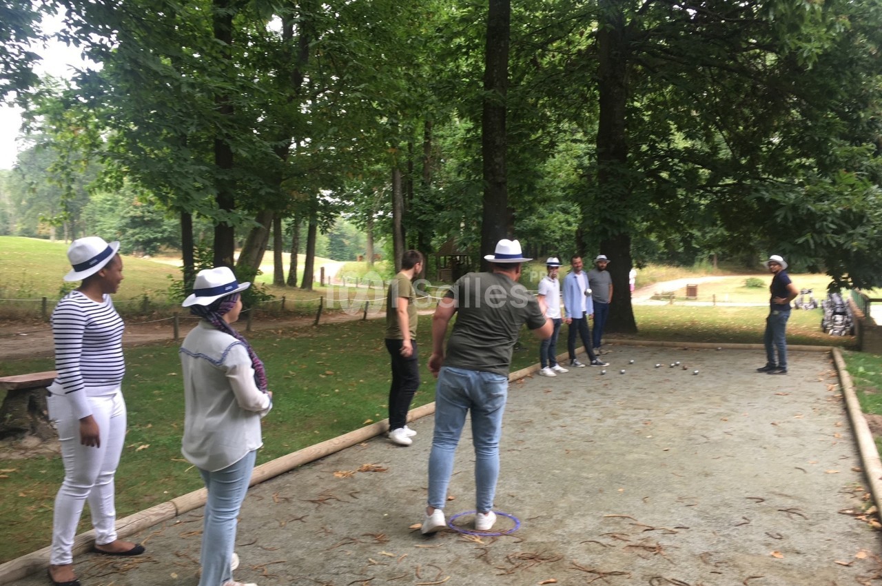 Des personnes jouent à la pétanque sur un terrain en plein air entouré d'arbres dans un parc.