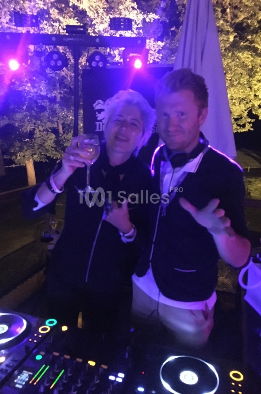 Deux personnes souriantes derrière une table de mixage éclairée, dans une ambiance nocturne festive.