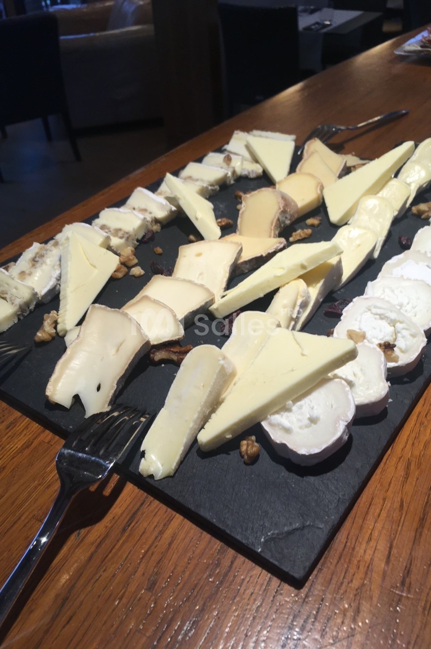 Plateau de fromages variés disposés sur une ardoise avec des fourchettes, présenté sur une table en bois.