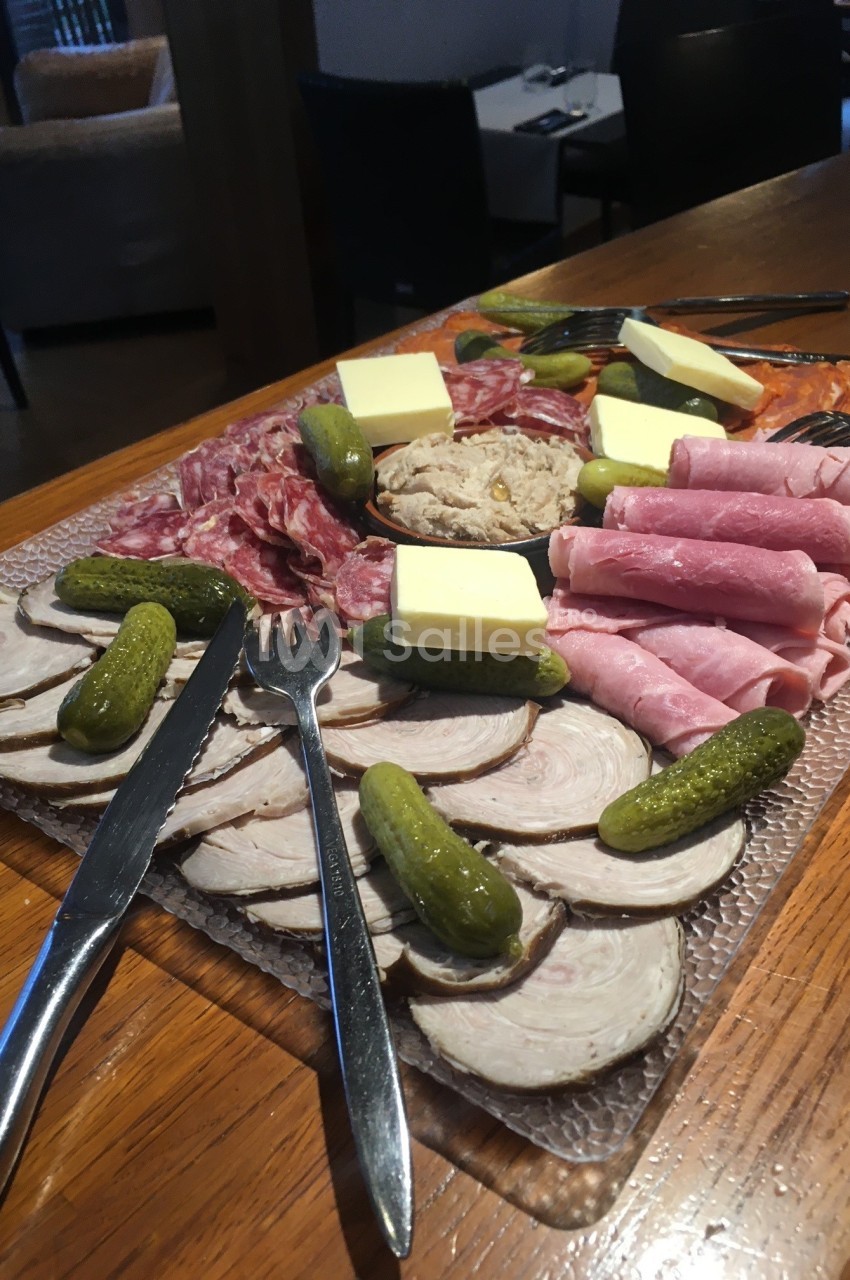 Plateau de charcuterie variée avec cornichons, beurre, pâté et tranches de jambon et saucisson sur une table en bois.