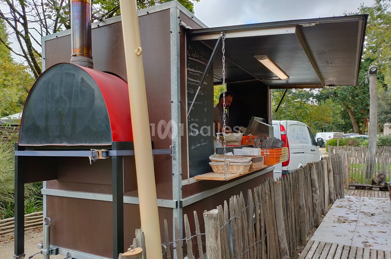 Four à bois mobile dans une remorque aménagée, entourée d'une clôture en bois, avec un cuisinier à l'intérieur.