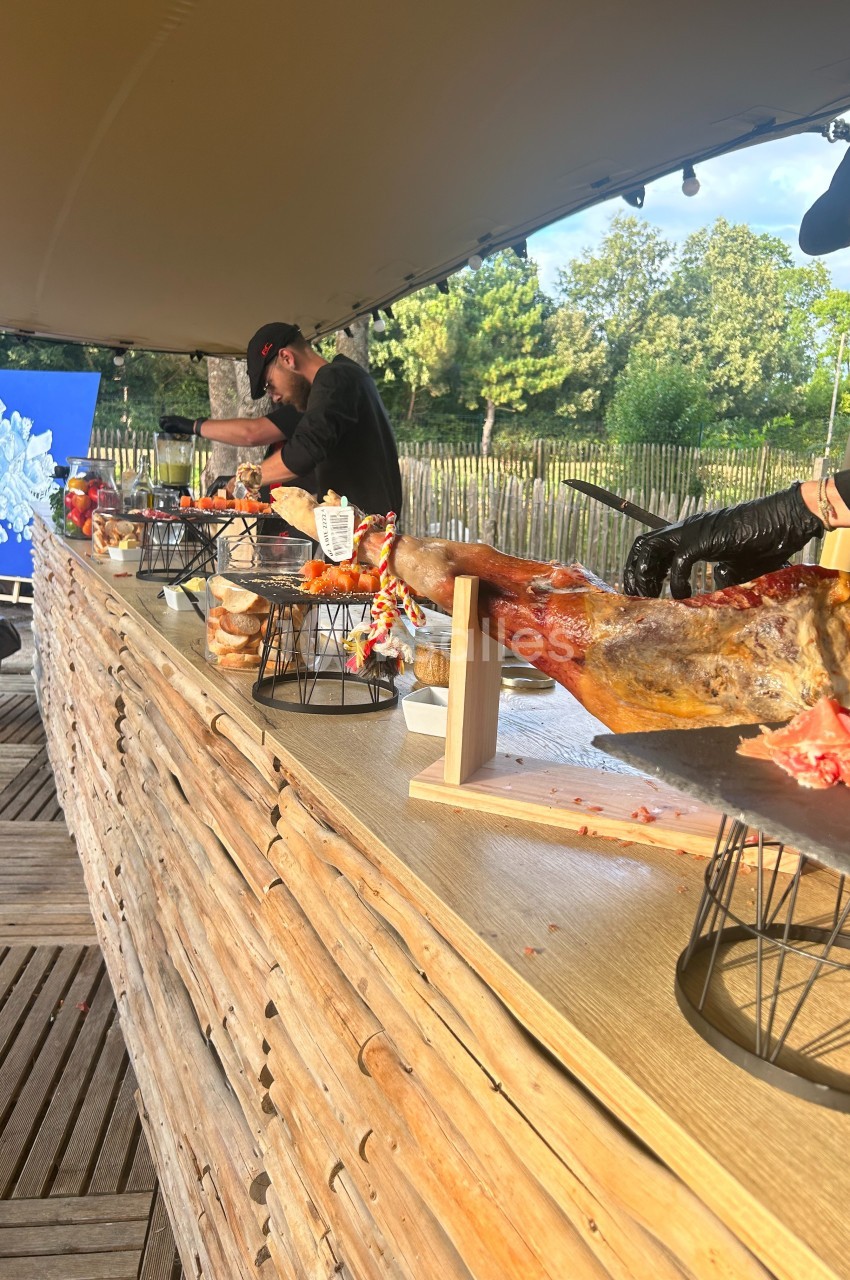 Des cuisiniers découpent des jambons sur un comptoir en bois lors d'un événement en plein air.