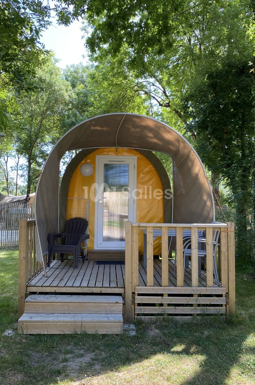 Hébergement insolite en forme de tente avec terrasse en bois, entouré d'arbres et situé dans un espace naturel.