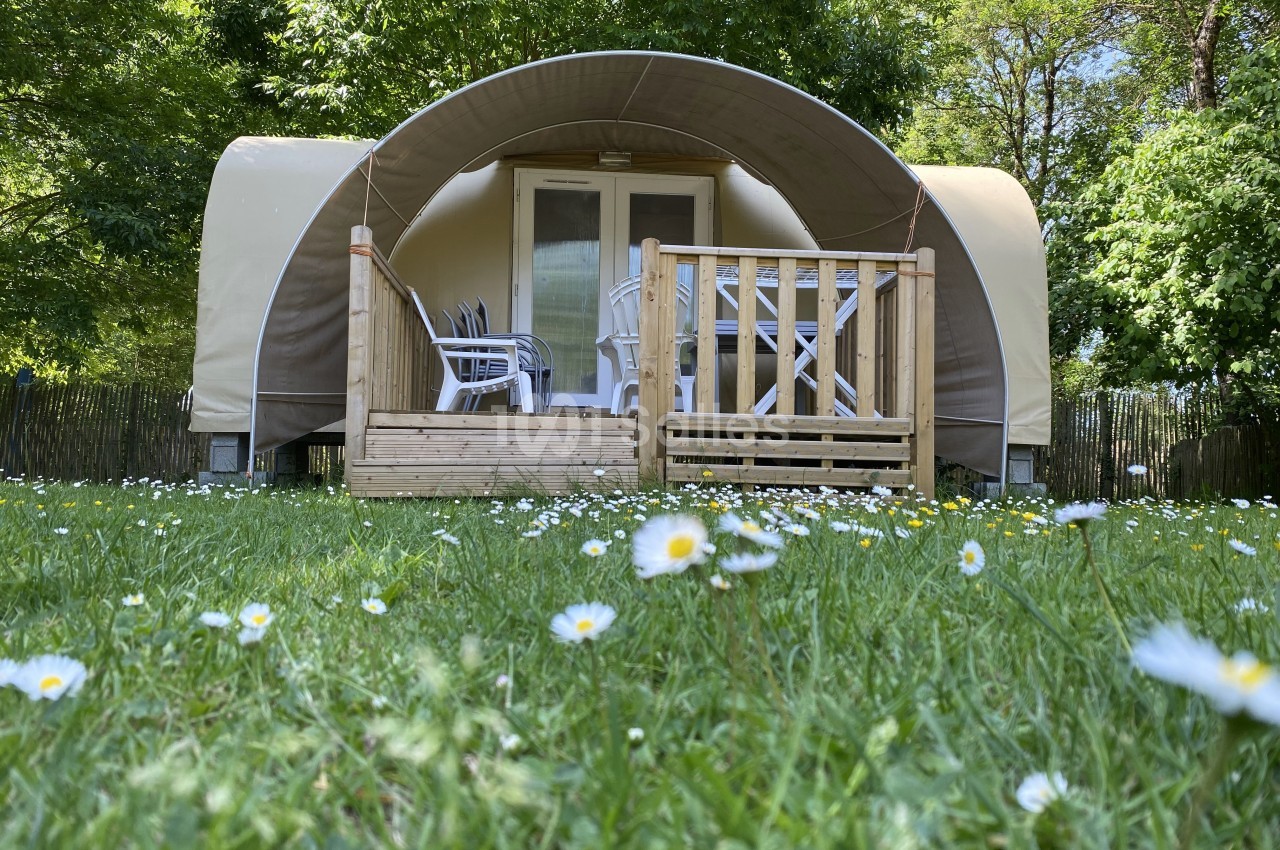 Hébergement en toile et bois avec terrasse, entouré de verdure et de fleurs blanches dans un cadre naturel.
