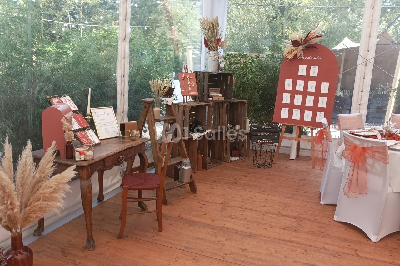 Décoration de mariage avec table en bois, cagettes, épis de blé, plan de table et chaises décorées dans une salle lumineuse.