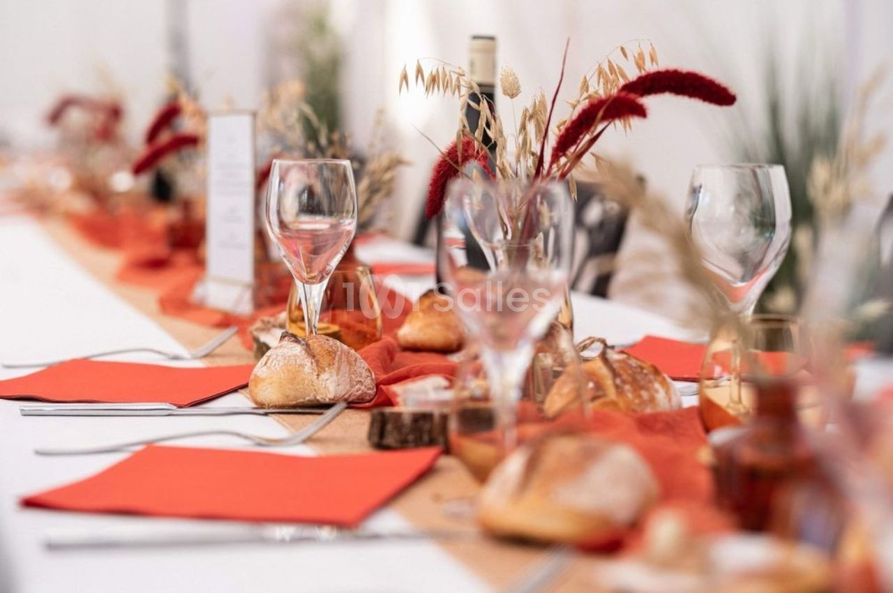 Table dressée avec des verres, du pain, des serviettes rouges et une décoration automnale avec des fleurs séchées.