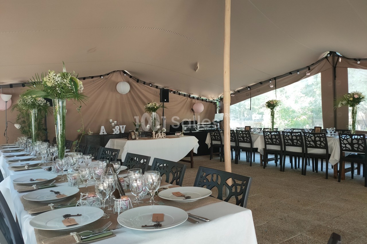 Salle de réception décorée pour un événement, avec tables dressées, nappes blanches et arrangements floraux.