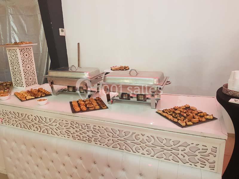 Buffet avec plats chauds dans des chafing dishes et assortiments de bouchées disposés sur un comptoir décoratif blanc.