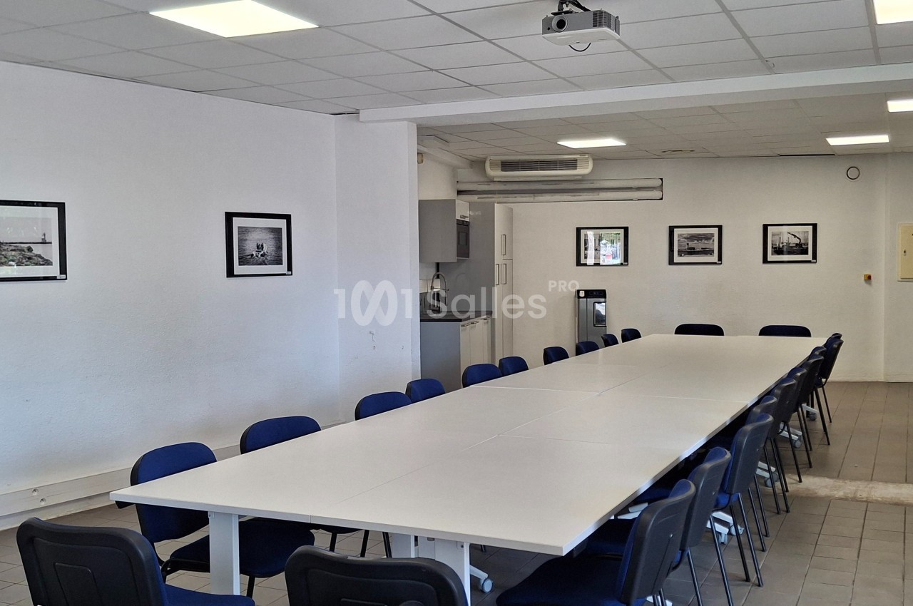 Salle de réunion lumineuse avec une grande table rectangulaire entourée de chaises, murs blancs décorés de cadres.