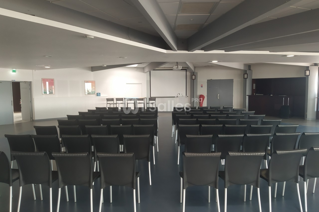Salle de conférence vide avec des rangées de chaises noires alignées face à un écran et un pupitre.