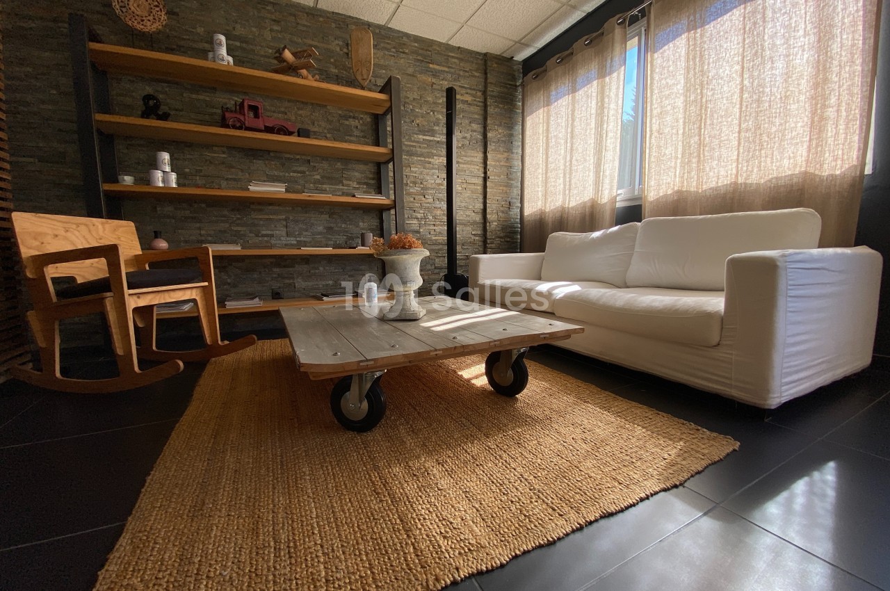 Salon lumineux avec canapé blanc, table basse en bois sur roulettes, fauteuil à bascule et étagères en fond.