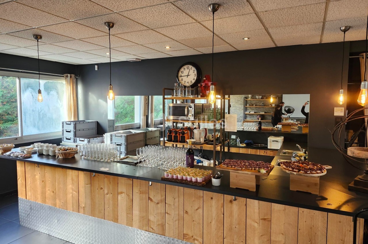 Comptoir en bois avec verres, amuse-bouches et bouteilles, dans une salle lumineuse au décor moderne et industriel.