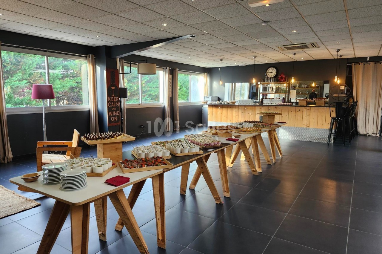 Salle lumineuse avec buffet dressé sur des tables en bois, offrant divers plats et desserts dans un cadre moderne.