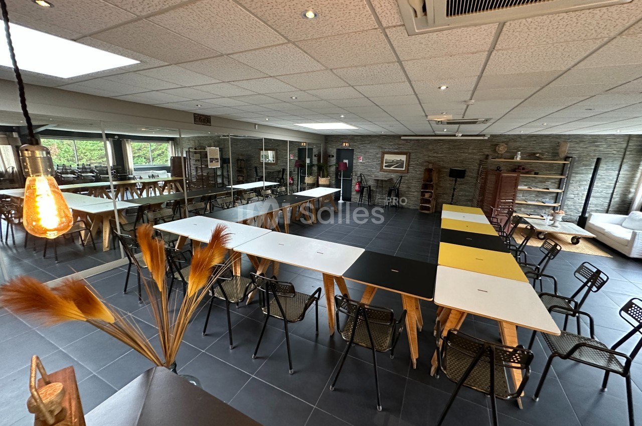 Salle de réunion moderne avec tables disposées en U, chaises noires, éclairage chaleureux et grandes baies vitrées.