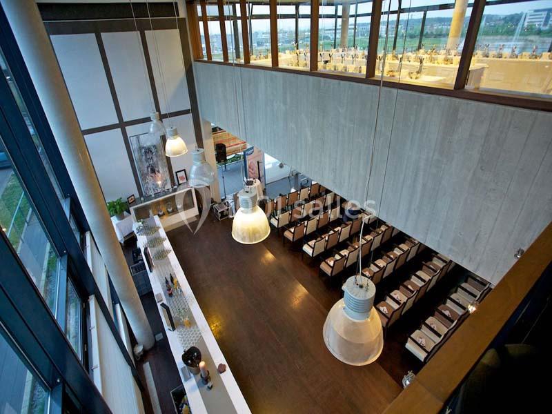 Vue d'ensemble d'un restaurant moderne avec un bar en bois, des tables alignées et de grandes baies vitrées.