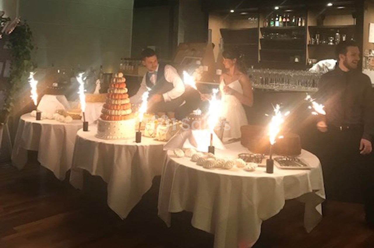 Des tables décorées avec des desserts, des fontaines lumineuses et des convives en tenue de fête dans une salle éclairée.