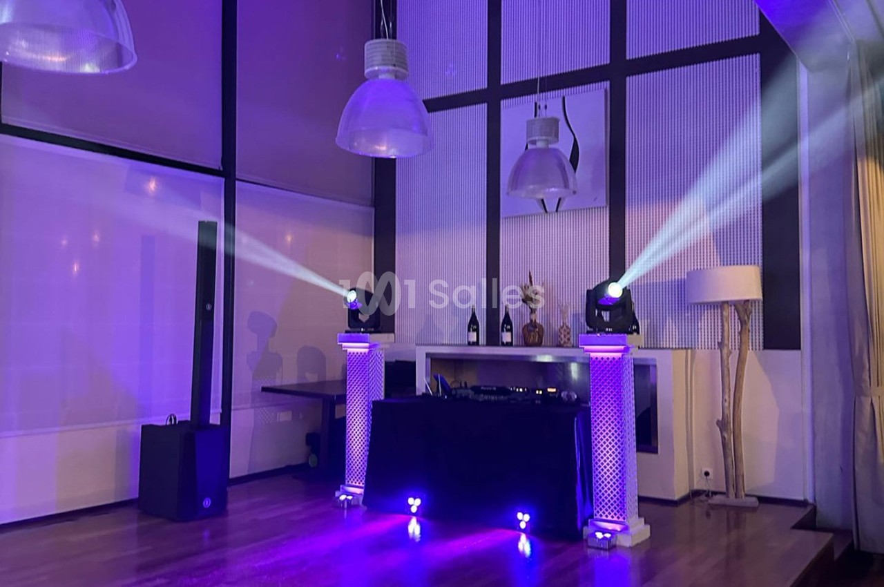 Salle de réception avec éclairage violet, projecteurs sur colonnes et équipement de sonorisation sur une table.