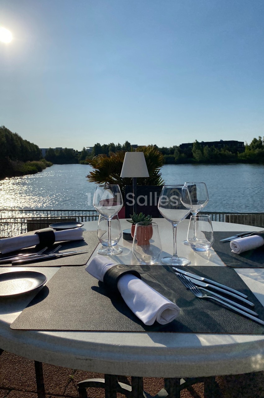 Table dressée avec élégance en extérieur, vue sur un lac ensoleillé et végétation en arrière-plan.