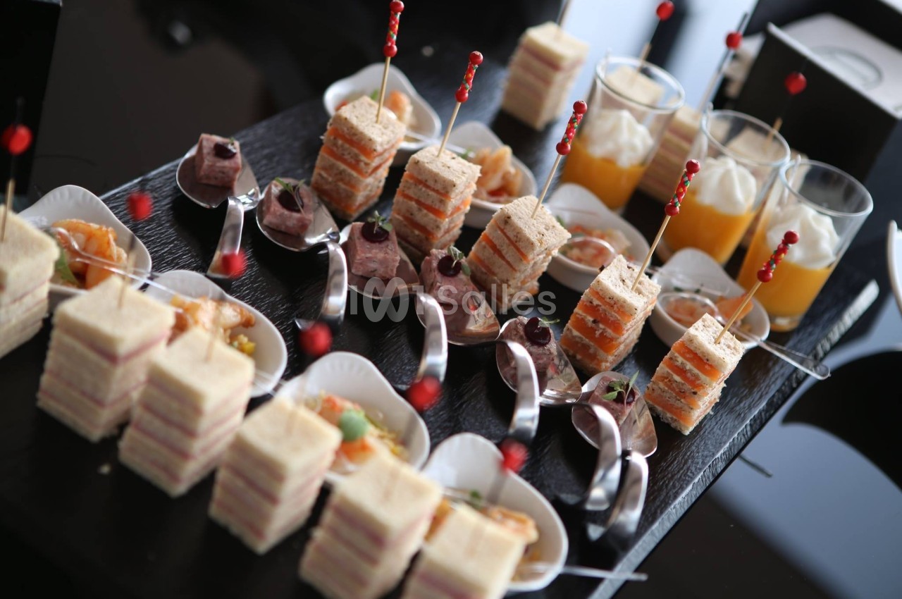 Plateau de bouchées apéritives comprenant mini-sandwichs, verrines et cuillères garnies, présenté sur une table noire.