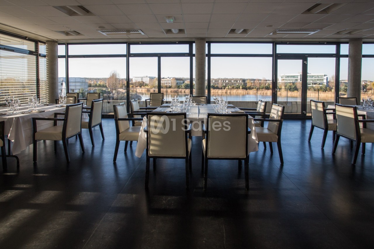 Salle de restaurant moderne avec grandes baies vitrées offrant une vue sur un paysage urbain et un cours d'eau.