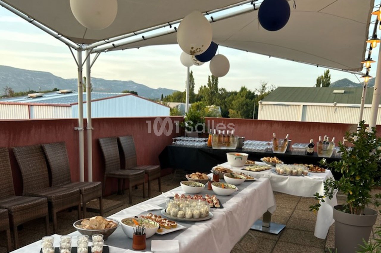 Buffet en extérieur sous une tente avec des plats variés, des boissons et une vue sur des montagnes en arrière-plan.