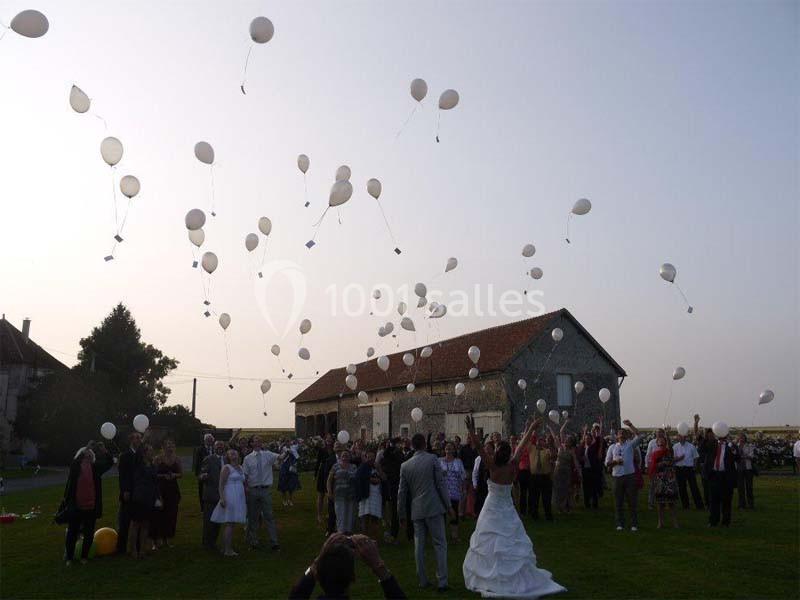 Groupe de personnes dans un jardin lâchant des ballons blancs dans le ciel près d'un bâtiment en pierre.