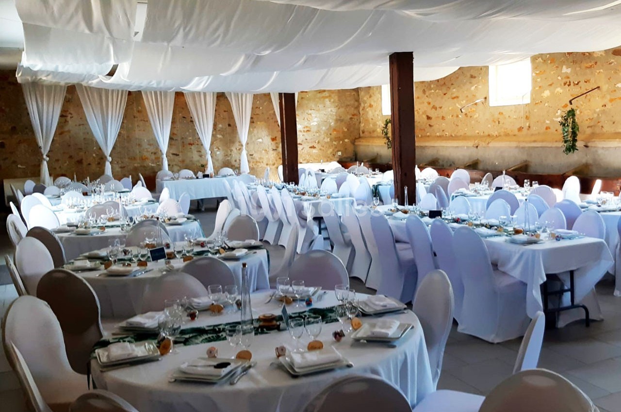 Salle de réception décorée avec des tables rondes dressées, nappes blanches et plafond drapé de tissu clair.