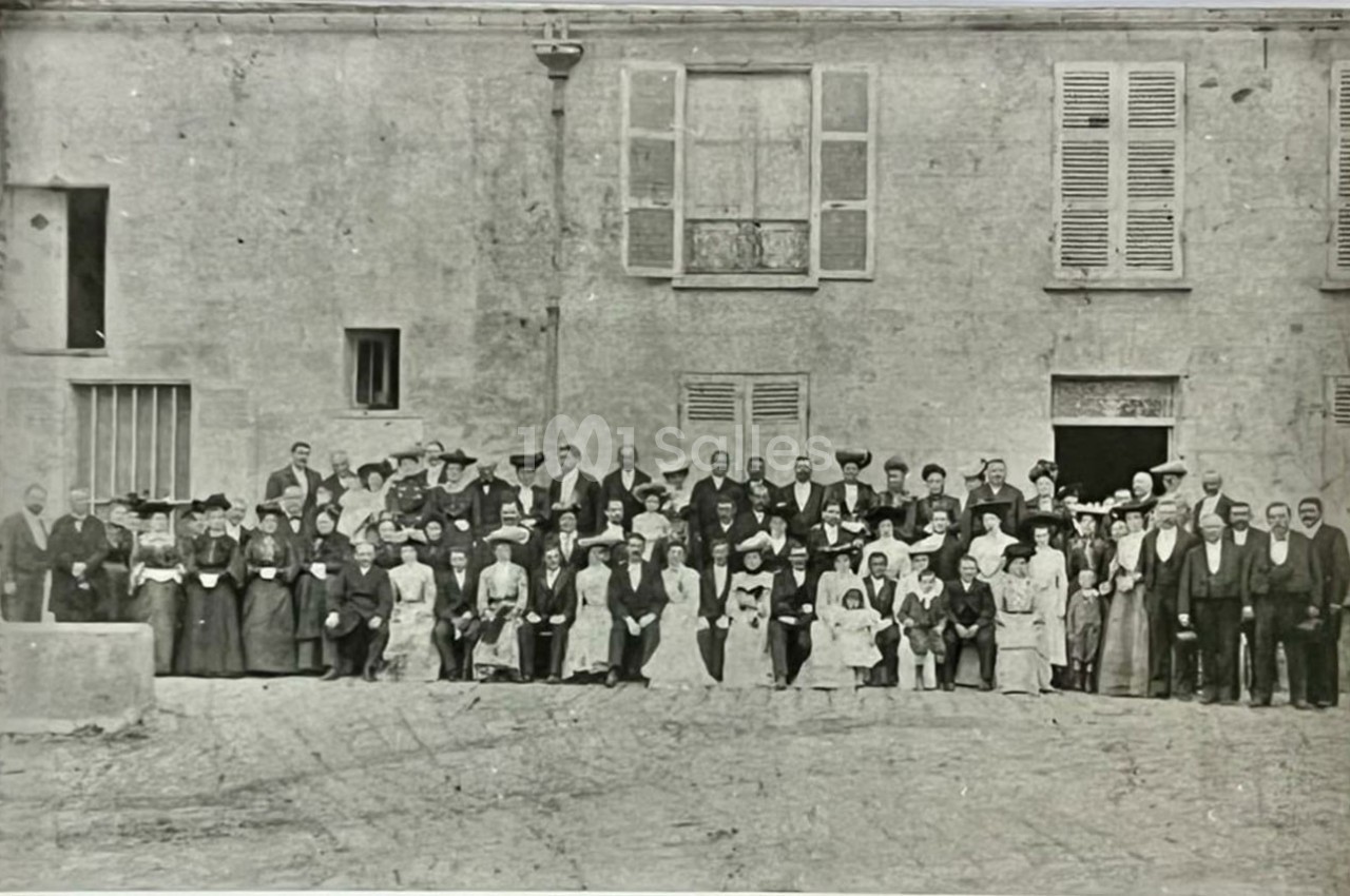 Photo en noir et blanc d'un grand groupe de personnes posant devant un bâtiment ancien avec des fenêtres et des volets.
