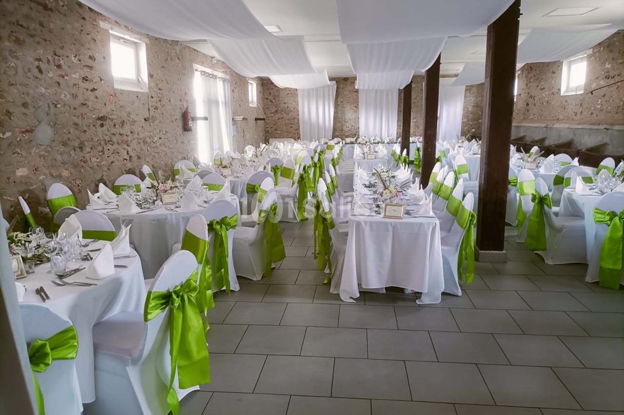 Salle de réception décorée avec des nappes blanches et des chaises ornées de nœuds verts, prête pour un événement.