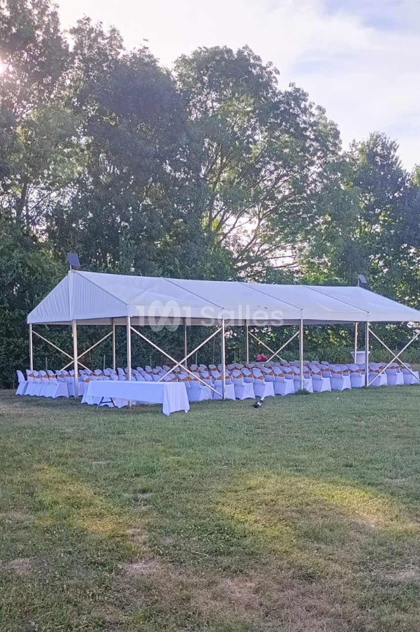 Tente blanche installée sur une pelouse, abritant des tables et chaises alignées pour un événement en plein air.