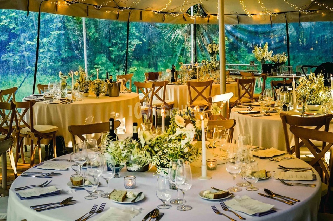Salle décorée pour un événement avec des tables rondes dressées, des fleurs blanches et un éclairage chaleureux.