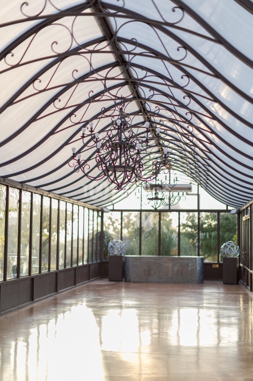 Intérieur d'une serre lumineuse avec un toit en verre, des lustres suspendus et un sol réfléchissant.
